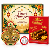 A gold Ganesh kumkum dish, silver coin, and red box of wafer rolls in front of a festive hamper box.