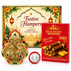 A gold Ganesh kumkum dish, silver coin, and red box of wafer rolls in front of a festive hamper box.