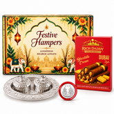 A festive gift hamper with a decorative box, red wafer rolls, a silver puja dish with two small containers, and a silver