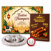 A festive hamper box, chocolate cigar rolls, a silver kumkum dish, and a Lakshmi-Ganesh coin on a white background.