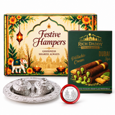 A festive gift box, pistachio wafer rolls, a silver kumkum dish, and a Lakshmi-Ganesh coin on a white surface.