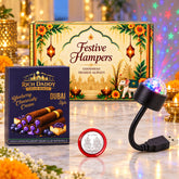 A festive gift hamper box, blueberry cream wafer rolls, a USB galaxy light, and a silver coin on a reflective surface.
