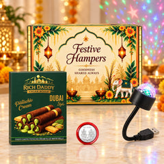 A festive gift hamper box, pistachio cream cigar rolls, a silver coin, and a USB galaxy light on a table with glowing lights.