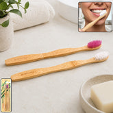 Two bamboo toothbrushes, one with pink bristles and one with white, on a bathroom counter with a person brushing their teeth
