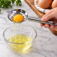 A hand holds a shiny stainless steel egg separator with a yolk inside, draining white into a clear bowl.