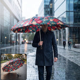 A man in a dark coat holds an open floral umbrella with red and white flowers on a dark green background, walking in the