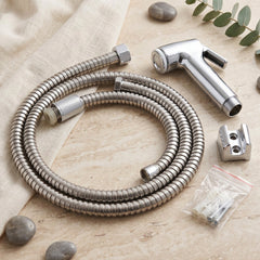 A coiled stainless steel hose, chrome bidet sprayer, wall mount, and screws on a light fabric and stone surface.