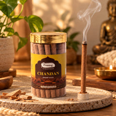 A lit brown dhoop stick emits smoke next to an open jar of similar sticks on a textured tray.