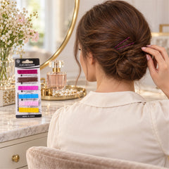 A woman with brown hair styled in a bun, secured with pink bobby pins, sits at a vanity with a package of colorful pins and