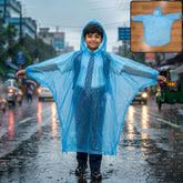 A young boy in a school uniform smiles while wearing a translucent blue poncho on a rainy city street.