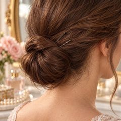 A close-up view from behind shows a woman's brown hair styled in a neat bun, secured with two grey bobby pins.