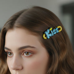 Close-up of four 'Kiss' text hair clips on a white background
