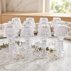 A group of twelve clear acrylic miniature table lamps arranged on a light-colored marble surface with delicate white flowers.