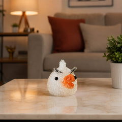 A white chick-shaped night lamp with an orange beak sits unlit on a marble coffee table in a living room setting.