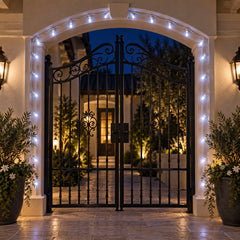 White LED string lights outlining an arched entryway with a large black wrought iron gate and sconces.