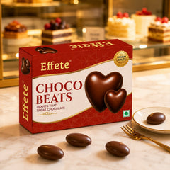 A box of Effete Choco Beats chocolates and three individual candies rest on a marble counter with a dessert display.