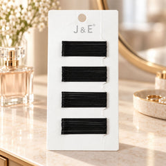 A white card holds four rows of black bobby pins on a vanity with perfume and a mirror.
