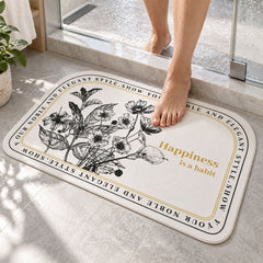 A person's bare feet step onto a half-round white mat with black floral print and a golden quote in a bathroom setting.