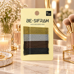 A yellow card holds four colors of bobby pins, next to a pearl bracelet and a vase of flowers.