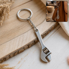 A silver metal mini adjustable wrench keychain with a key ring rests on a rustic wooden board.