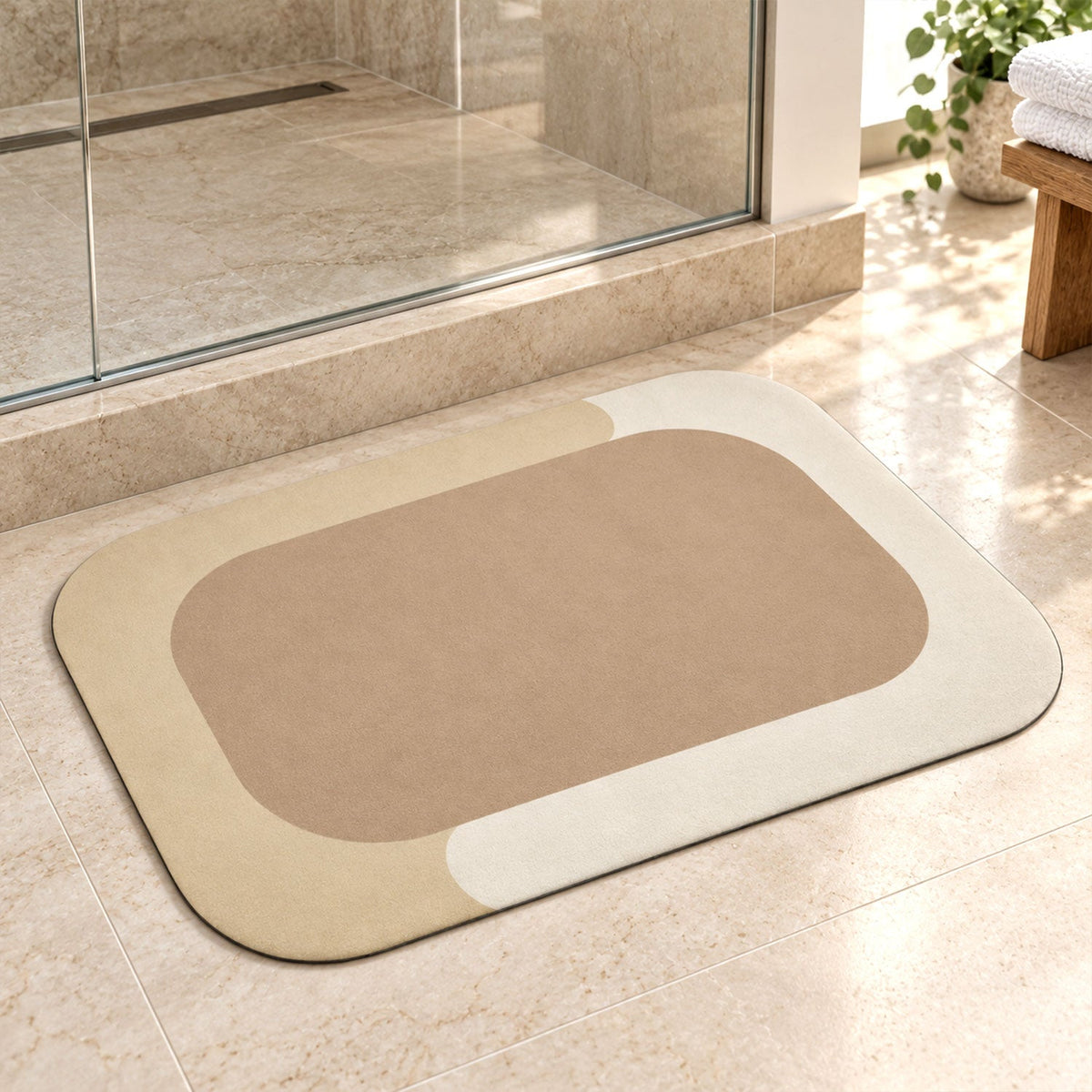 A rectangular bath mat with rounded corners, featuring a beige center and a light cream border, rests on tiled floor next to