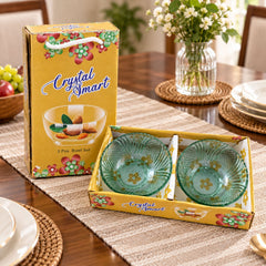 Two green glass bowls in a yellow box, with a vase of flowers and fruit on a wooden table.