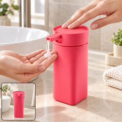 A person's hand presses a pink rectangular soap dispenser, releasing white liquid into another hand over a bathroom sink.