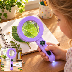 A child's hand holds a purple magnifying glass with an integrated compass and LED light, examining a green leaf on a
