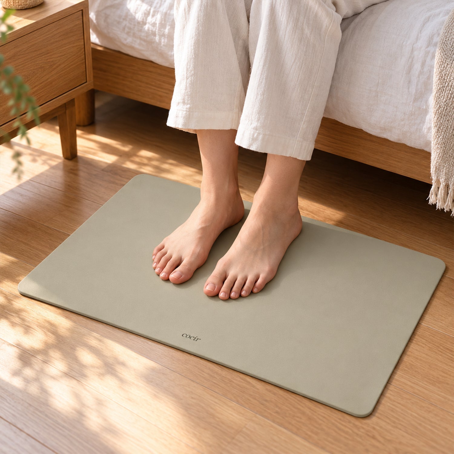 Bare feet stand on a light beige mat on a wooden floor beside a bed in a bedroom setting.