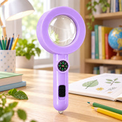 A purple magnifying glass with a compass and black switch stands upright on a wooden desk with an open book and colorful