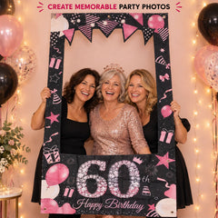 Three smiling women posing with a black and pink 60th birthday photo booth frame, surrounded by festive lights and balloons.