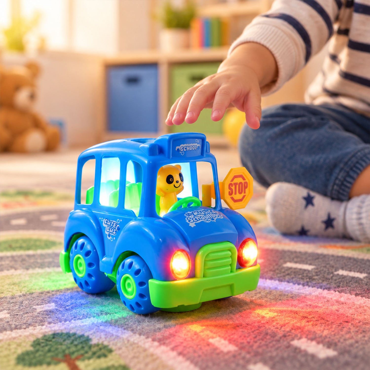 A child's hand reaches for a blue toy bus with glowing lights on a patterned rug.