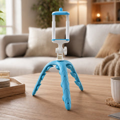 A blue and white flexible tripod for phones standing on a wooden coffee table in a modern living room setting.