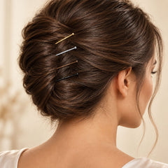 A woman's dark brown hair bun is styled with gold, silver, brown, and black bobby pins.