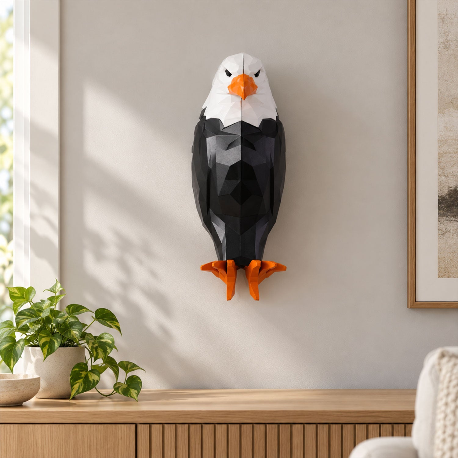 A geometric black and white eagle wall light mounted on a light gray wall above a wooden console table with a plant.