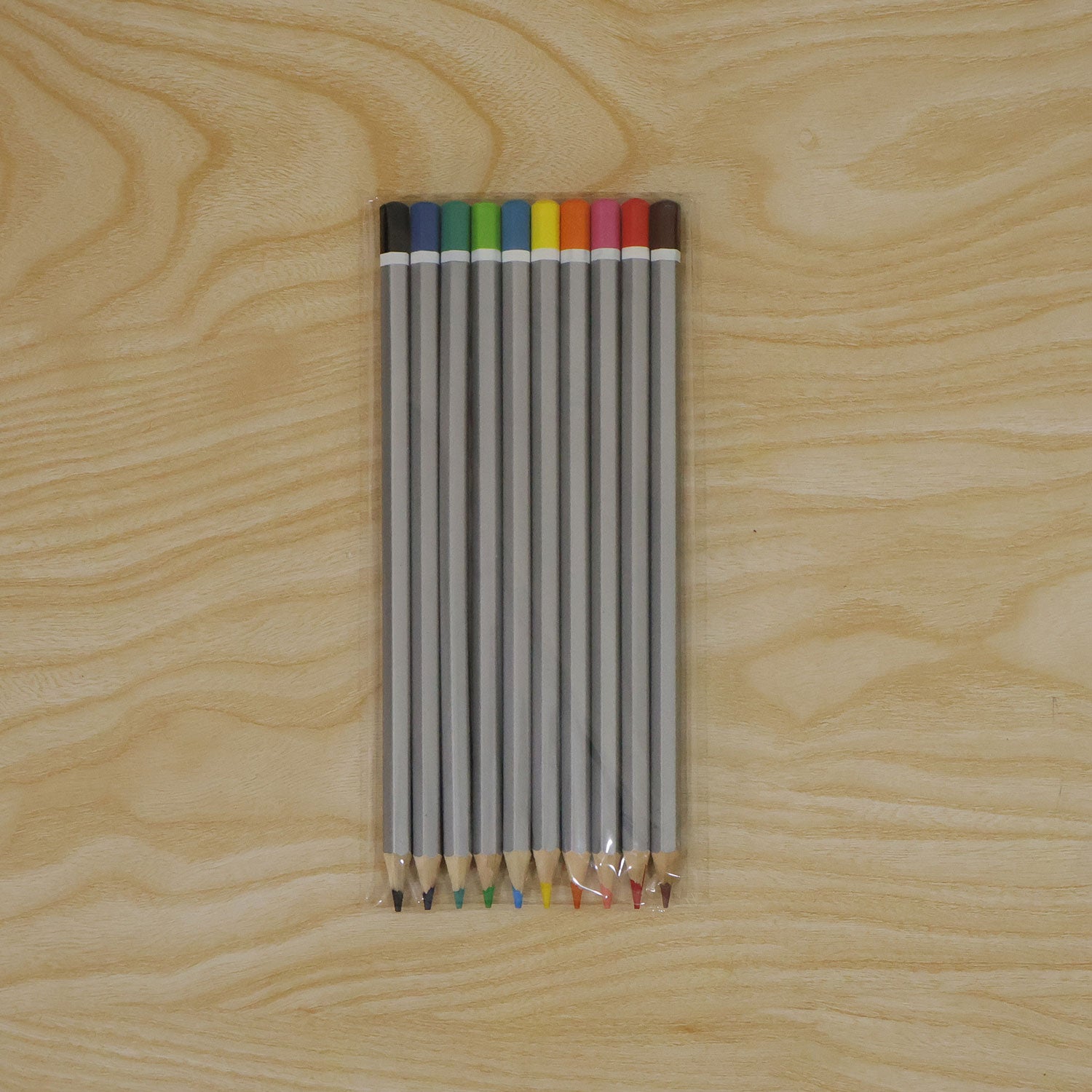 Ten gray hexagonal colored pencils with various tips and ends are sealed in clear plastic packaging on a light wooden