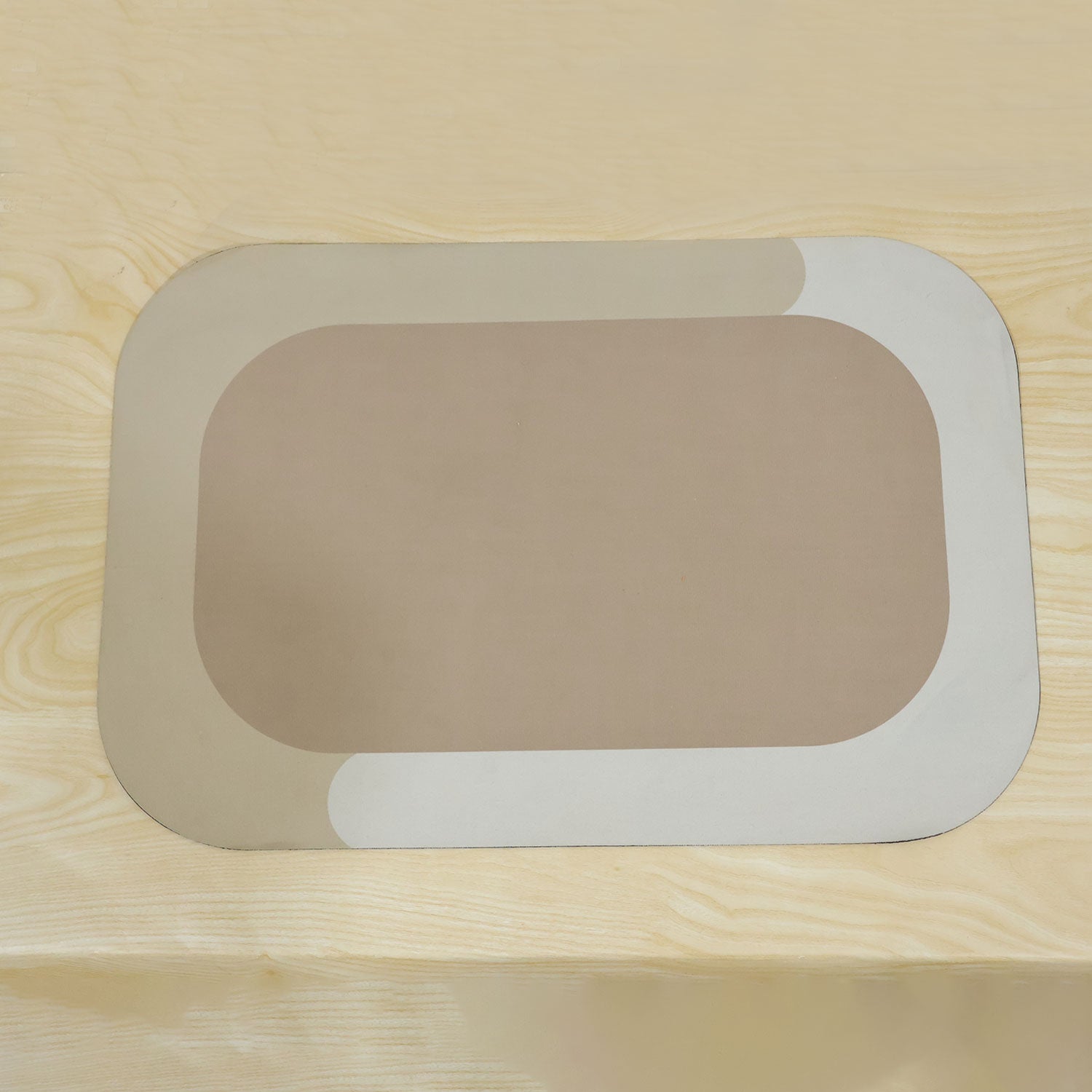 A rectangular bath mat with rounded corners, featuring a beige center and a light cream border, rests on a light wooden