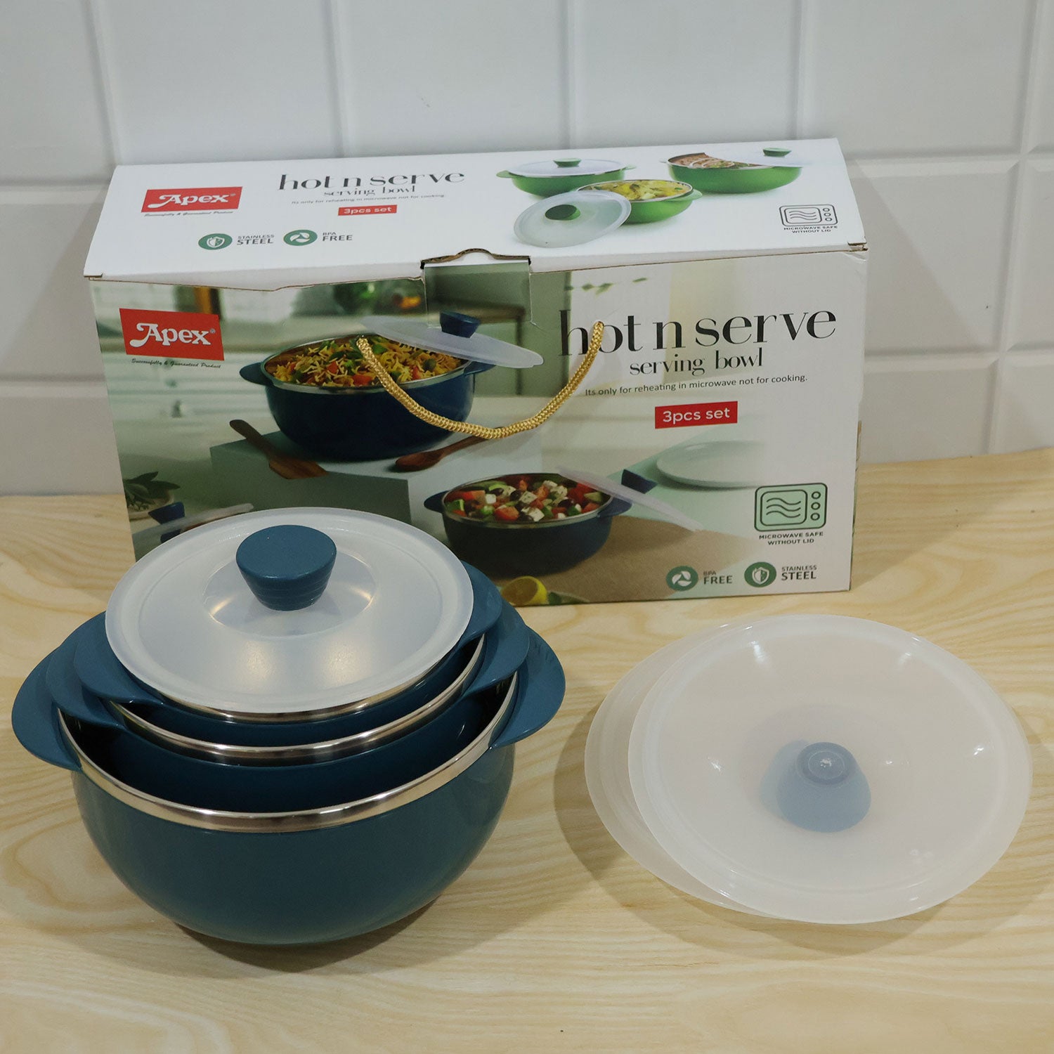 A stack of two blue serving bowls with clear lids sits next to a third lid and the product packaging box on a light wooden