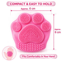 A pink paw-shaped scrubber with dimensions of approximately 6 cm by 6 cm and an illustration of it fitting in a hand.