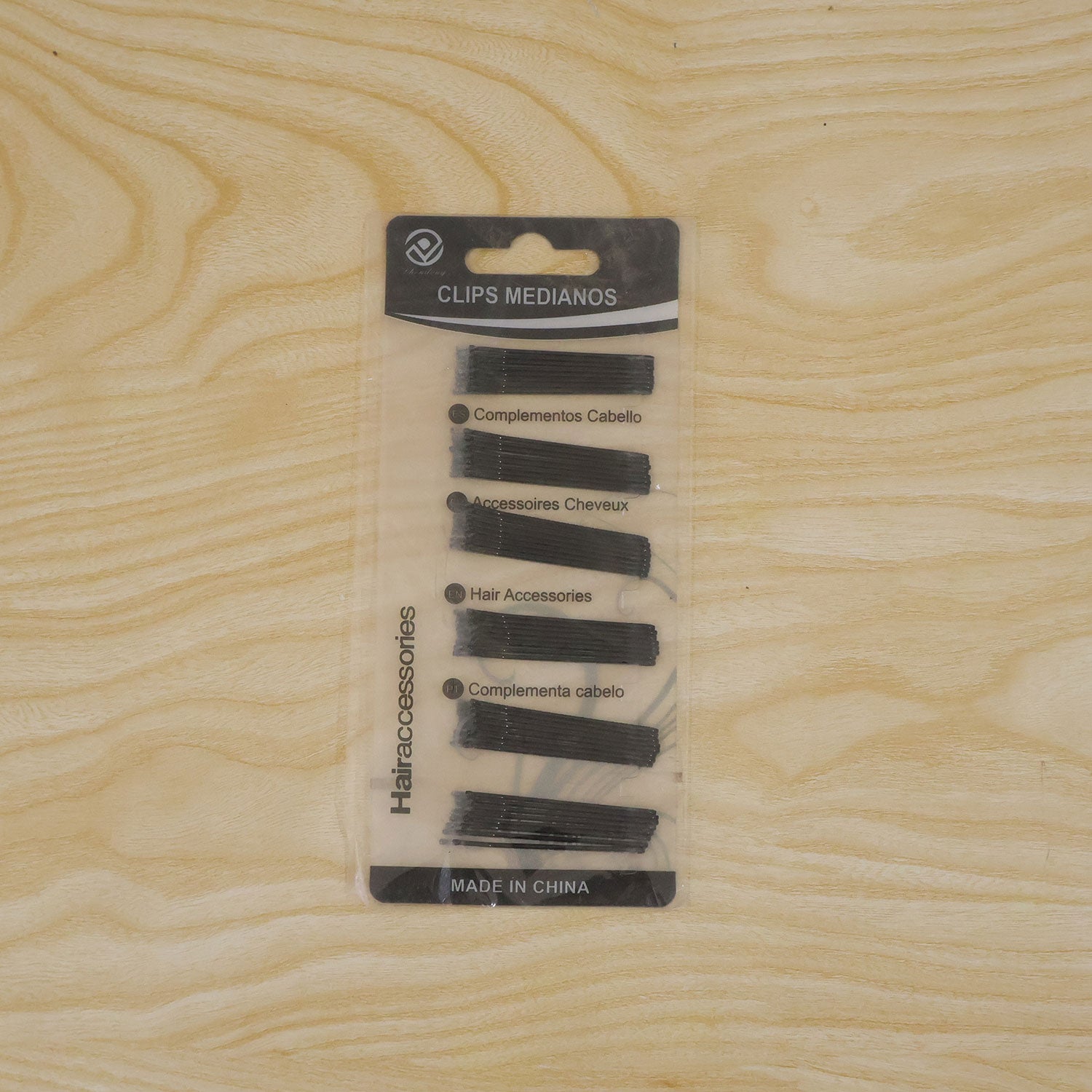 The packaged black U-shaped hair pins are displayed on a light wooden surface.