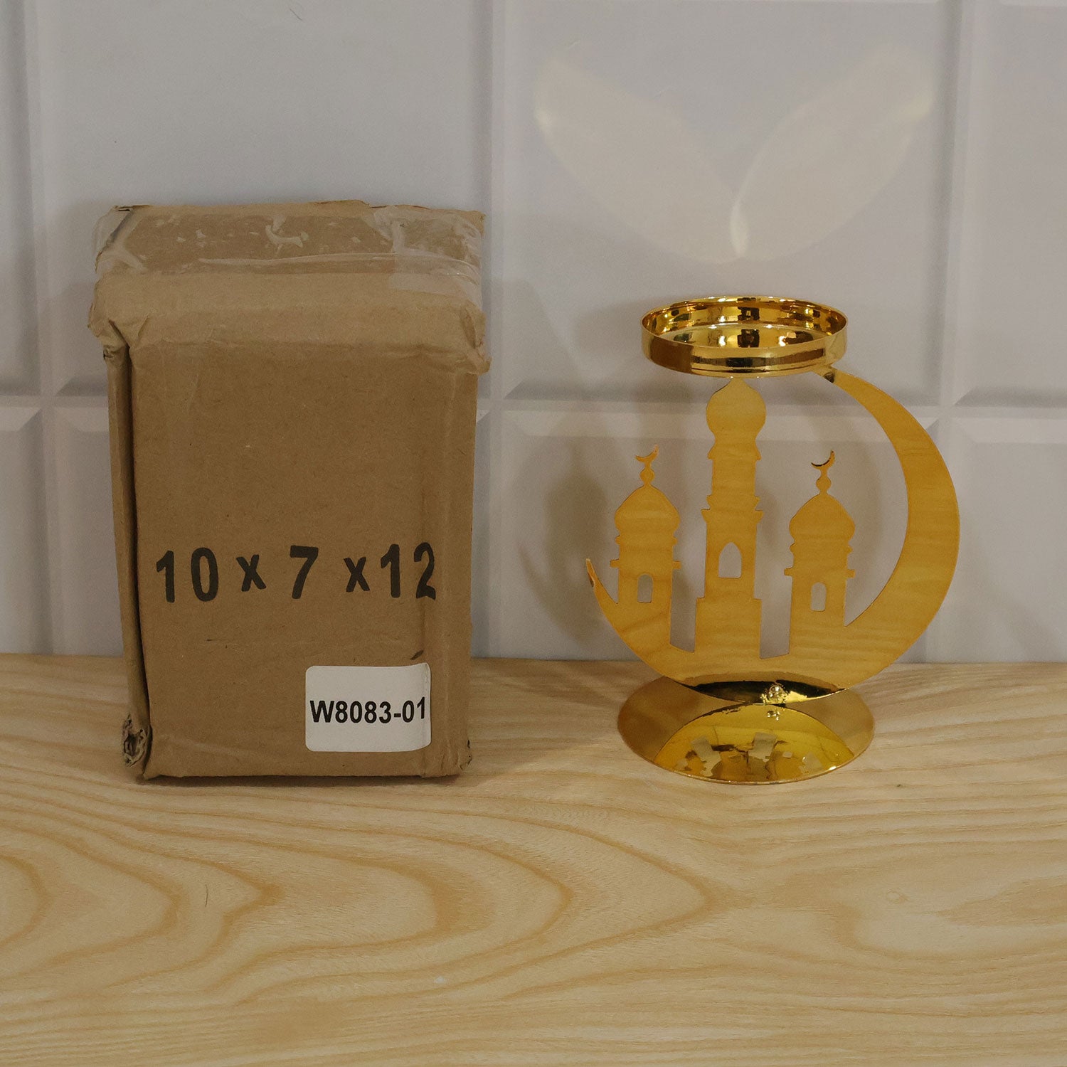 A golden metal incense holder with a crescent moon and mosque design, next to a brown cardboard box on a light wooden