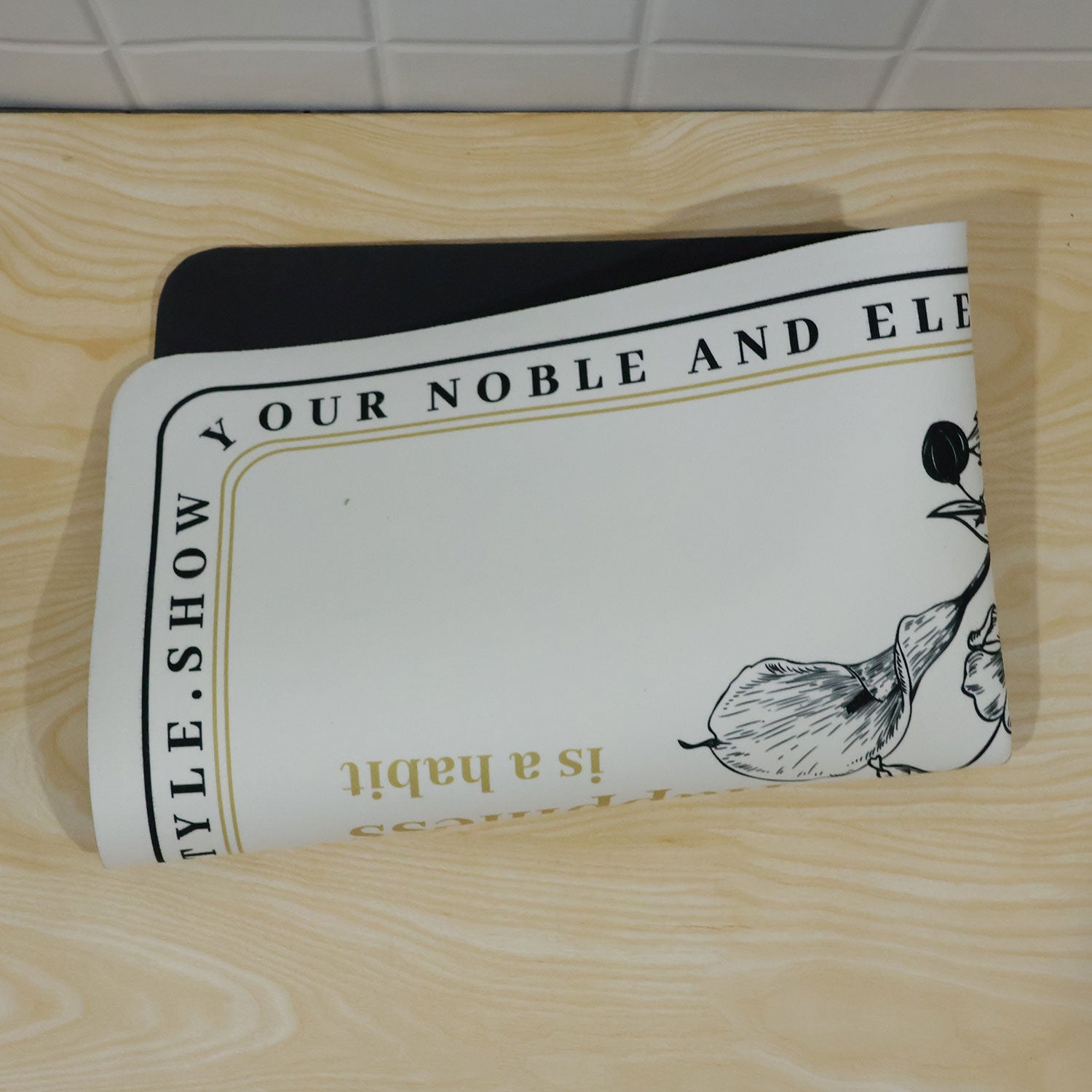 A half-round white mat with black floral print and a golden quote, folded on a light wooden surface.