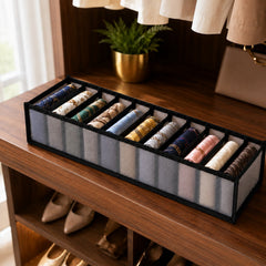A gray 11-section fabric organizer filled with rolled scarves and ties sits on a wooden shelf in a closet.