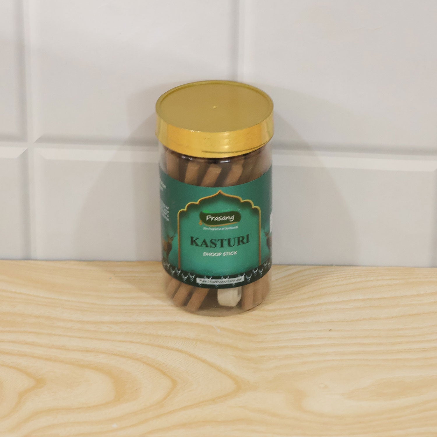A clear jar of dhoop sticks with a gold lid on a light wooden surface against white tiles.