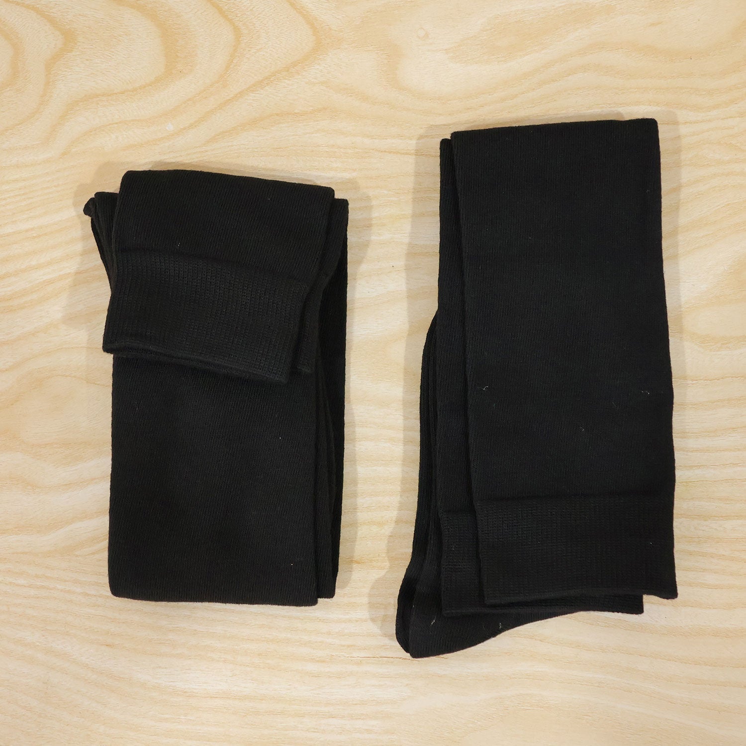 Two pairs of black over-knee socks, neatly folded and stacked, placed on a light wooden surface.