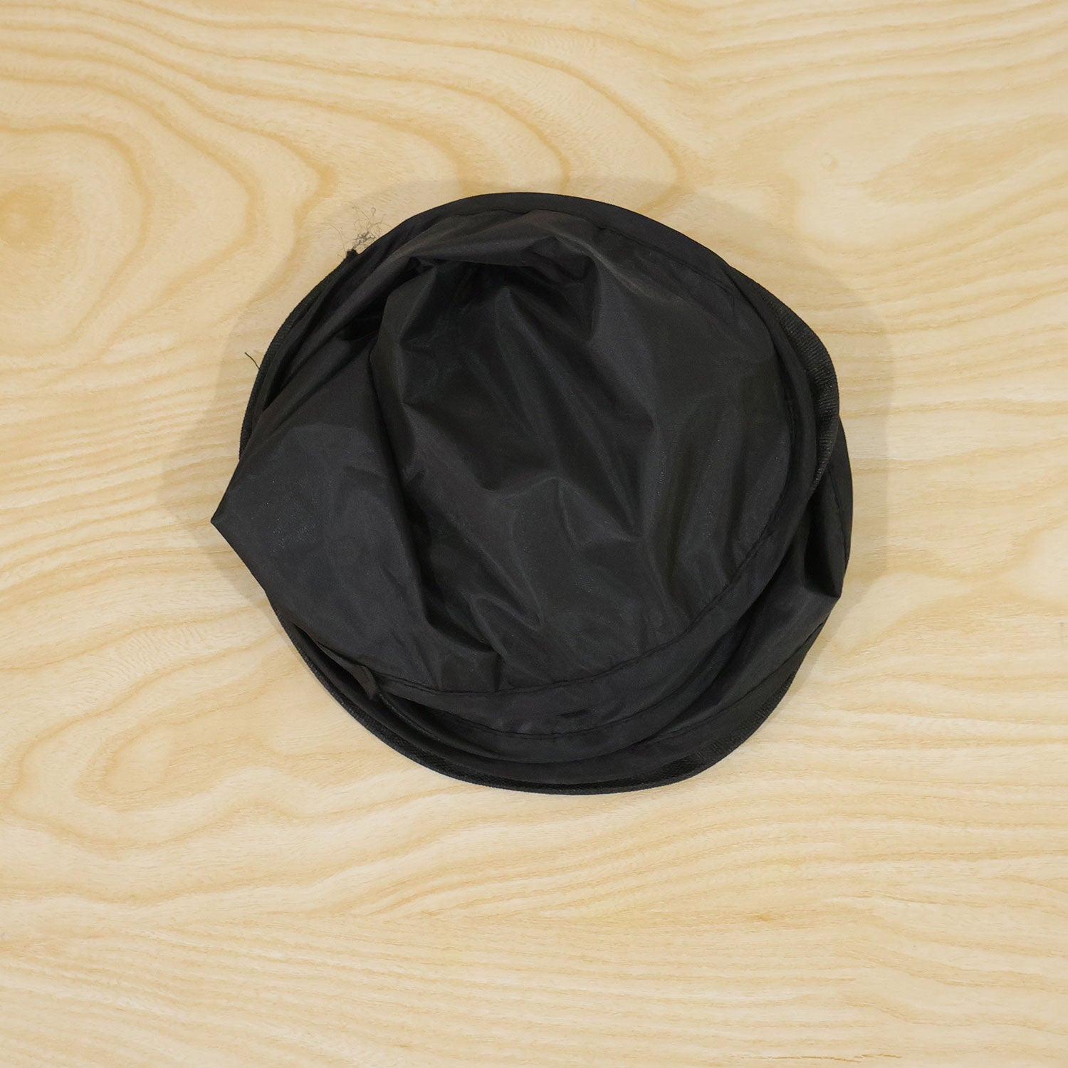 A single black car window sun shade folded into a compact, circular shape on a light wooden surface.