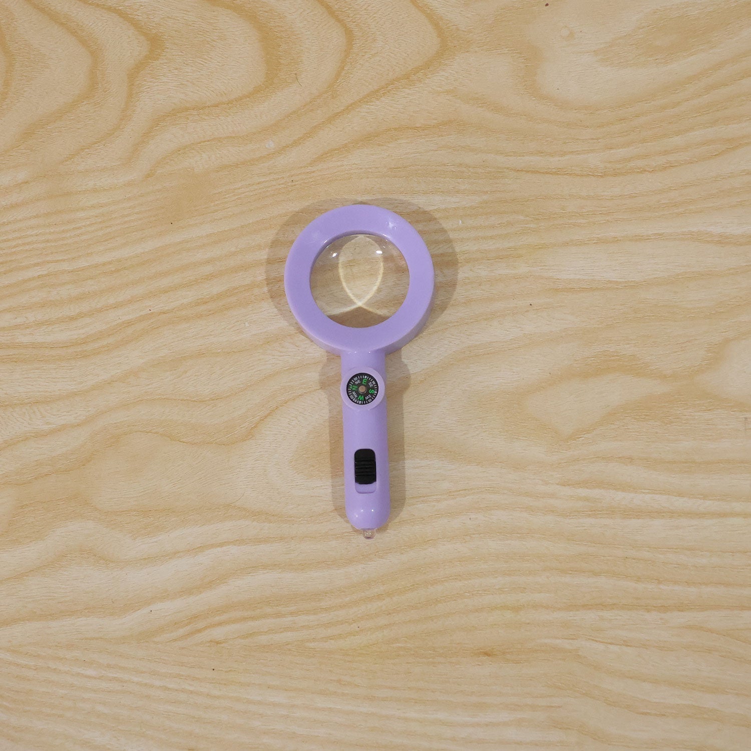 A purple magnifying glass with a compass and light is centered on a light-colored wooden surface with visible grain.
