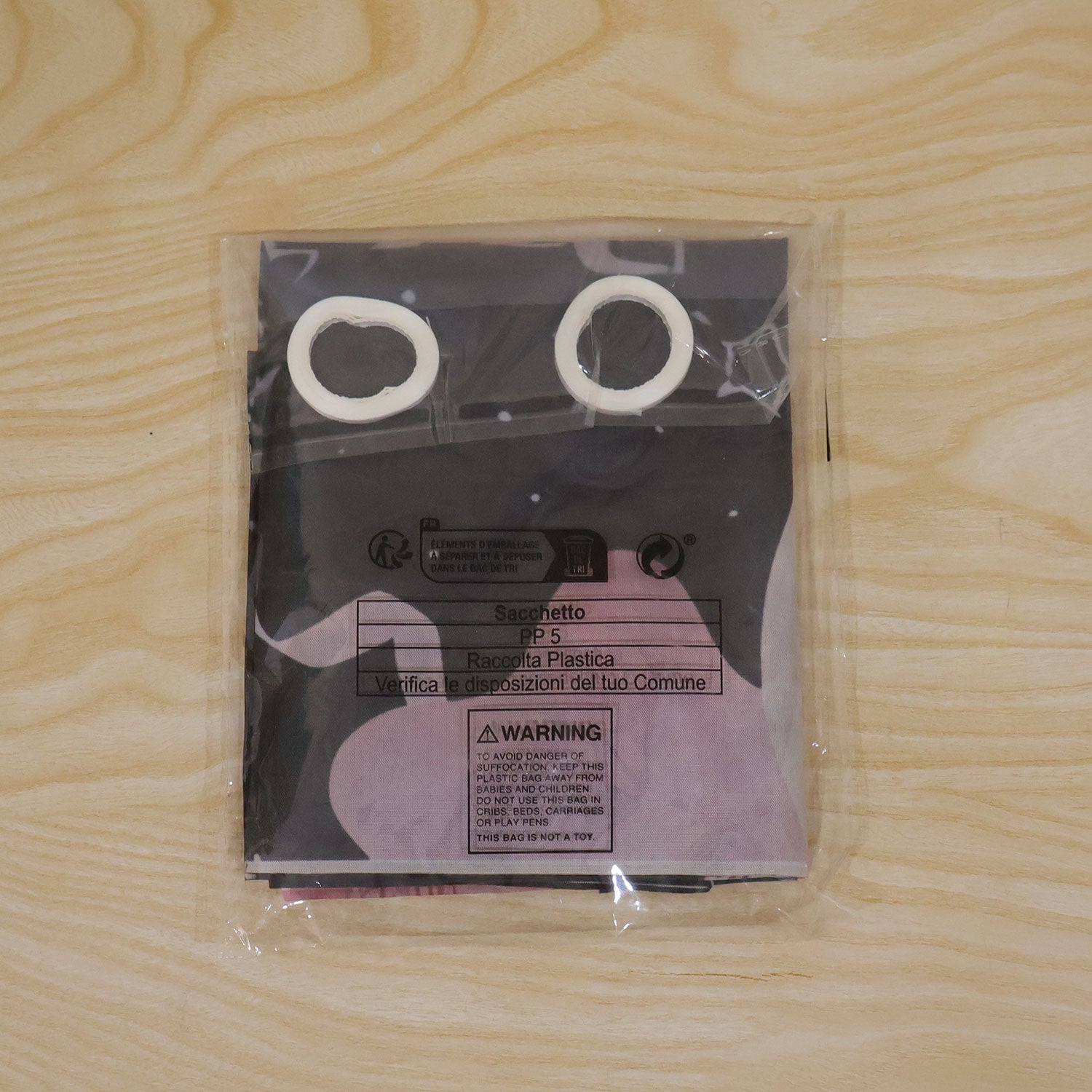 A clear plastic package containing the folded black and pink photo booth banner and two white hanging rolls on a wooden