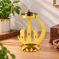A golden metal incense holder with a crescent moon and mosque design, holding a burning dhoop cone on a wooden table.