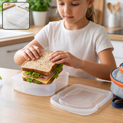 A child places a sandwich into a clear plastic container with its lid beside it on a wooden table.
